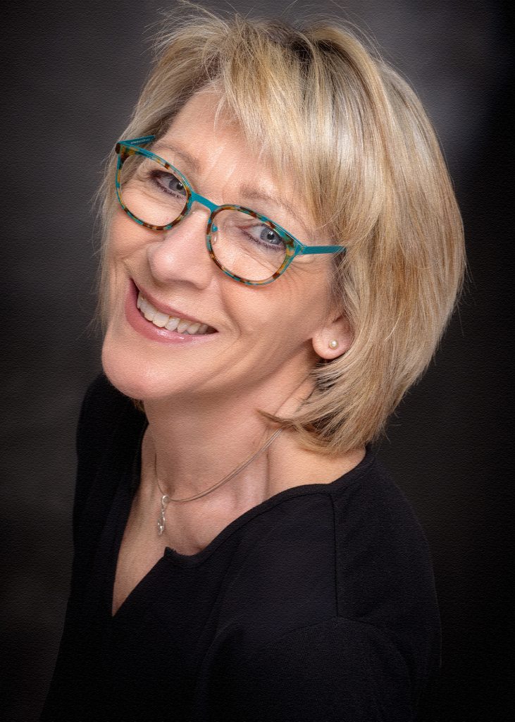 Bewerbungsfoto einer blonden Frau mit Brille und schwarzem Oberteil