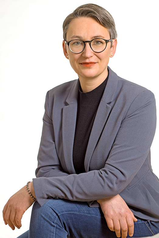 Bewerbungsfoto einer Frau mit kurzen Haaren und Brille, grauem Sakko und dunklem Rollkragenpullover und starker Persönlichkeit